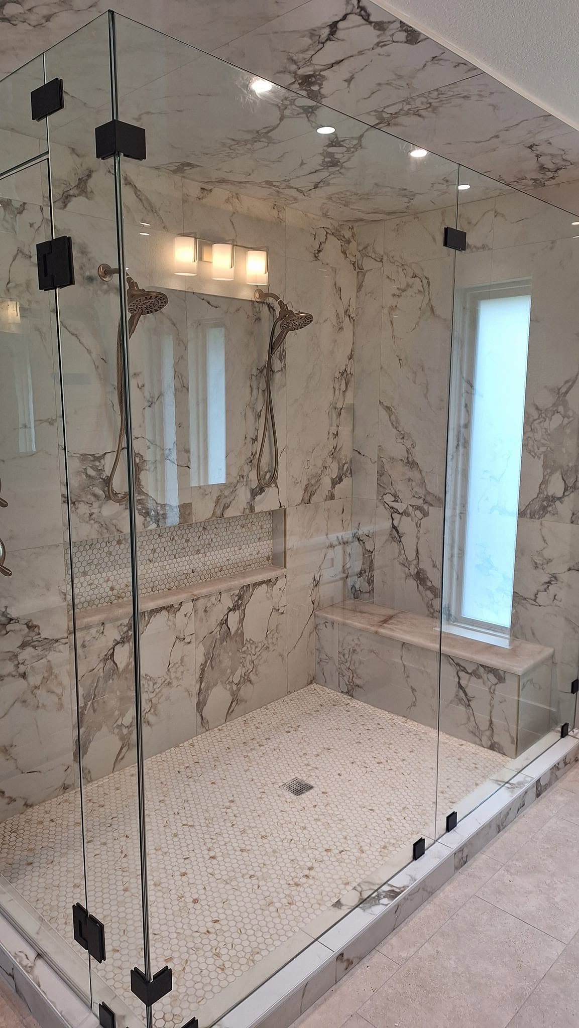 Large frameless shower enclosure with Calacatta tile and black hardware installed by Clearwater Glass and Showers